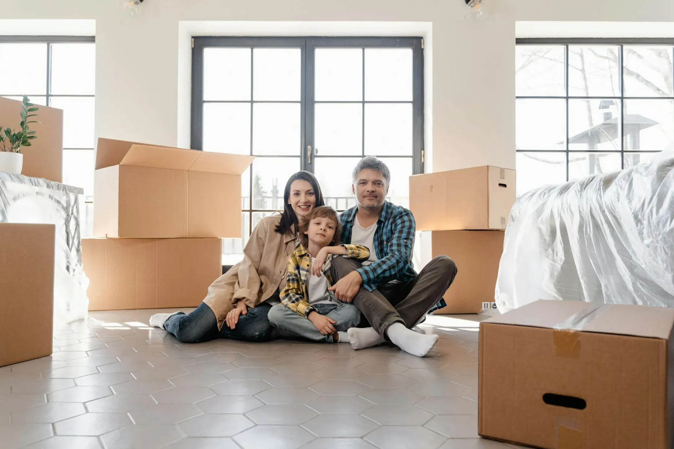 Homeowner in casual clothes kneeling under a kitchen sink with the power cord unplugged, holding an Allen wrench near the bottom of the disposal.