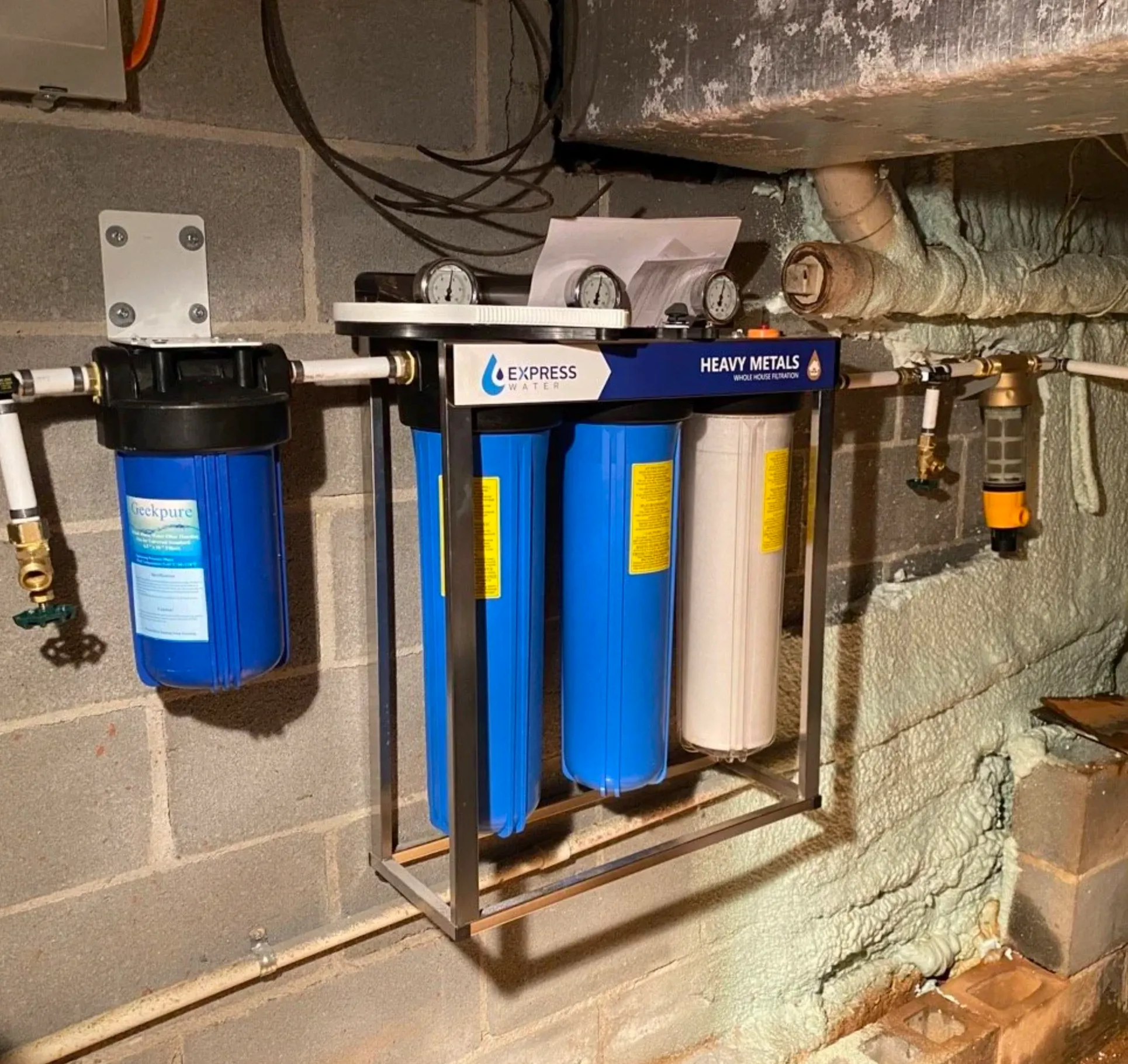 Neatly labeled whole-house filtration and water heater setup in a garage